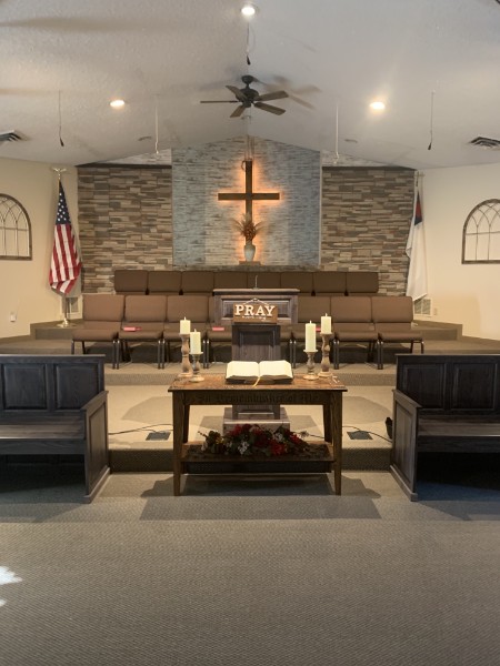 Faith Baptist Church sanctuary with a central pulpit, stone wall, wooden cross, and American flag.